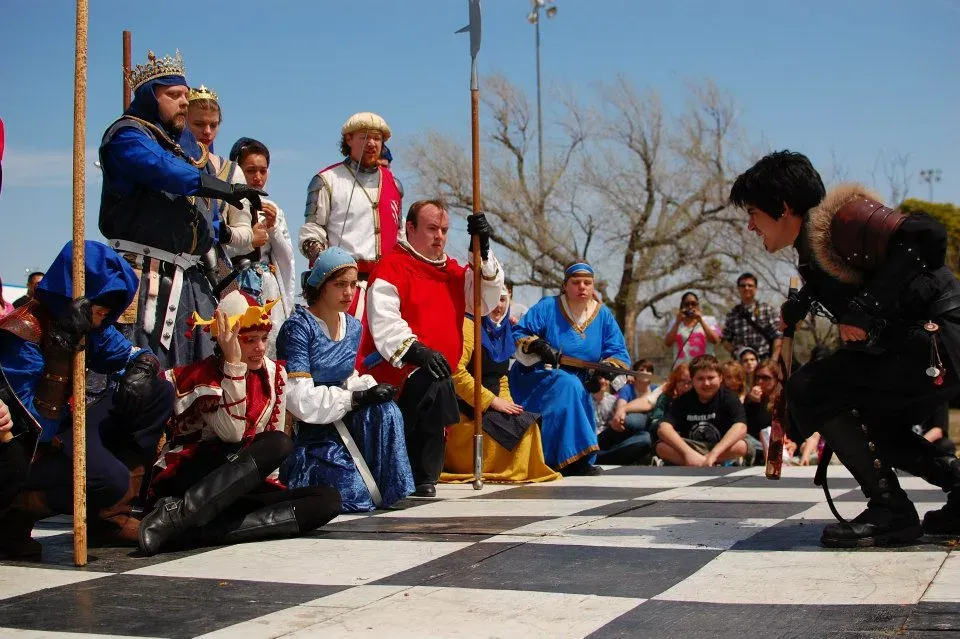 A staged two-weapon fight performed on a checkered stage in front of a crowd
