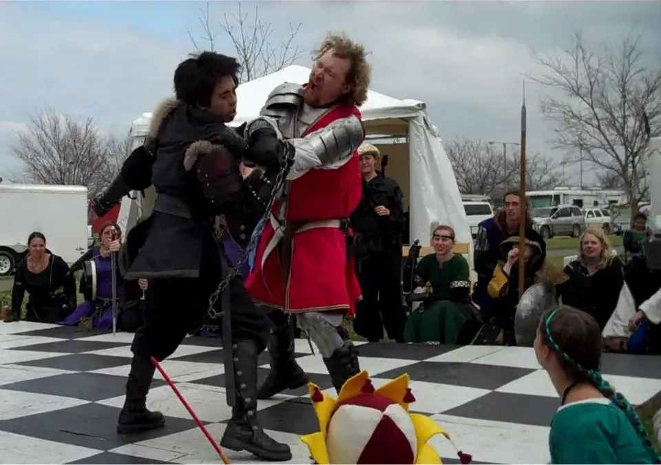 A staged sword fight between two costumed performers at an outdoor fair
