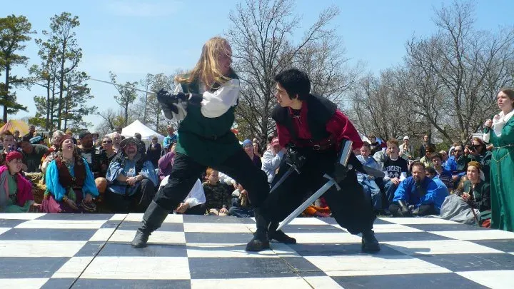 Two performers mid-exchange in a choreographed two-weapon fight